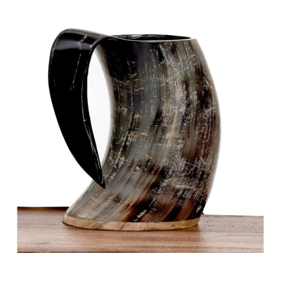 A ram horn drinking mug, a symbol of Aries, crafted from ethically sourced materials with a dark, textured finish and black handle, placed on a wooden surface.