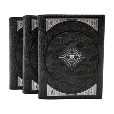 A black vegan leather journal with a rugged, textured cover featuring an intricate eye and crescent moon design, perfect for Aries to jot down ideas or passionate stories.