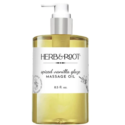 A bottle of Herb&Root spiced vanilla glaze cinnamon massage oil, 8.5 fl oz, with a pump dispenser, featuring golden liquid and a floral label design.