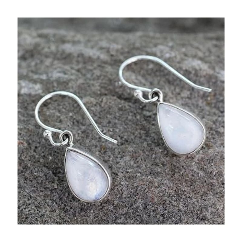 Image of two moonstone drop earrings with teardrop-shaped iridescent stones hanging from silver hooks, placed on a rough surface